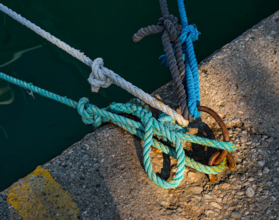 Mooring ring with tied blue and white nautical rope mounted on a concrete pier, marina safety equipment
